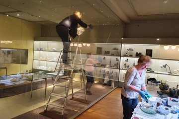 Moderne-Kuratorin Sabine Epple (auf der Leiter), Glas- und Keramikrestauratorin Ilona Faust (vorn) und Aufsichtspersonen bei der Reinigung der GRASSI-Sammlung