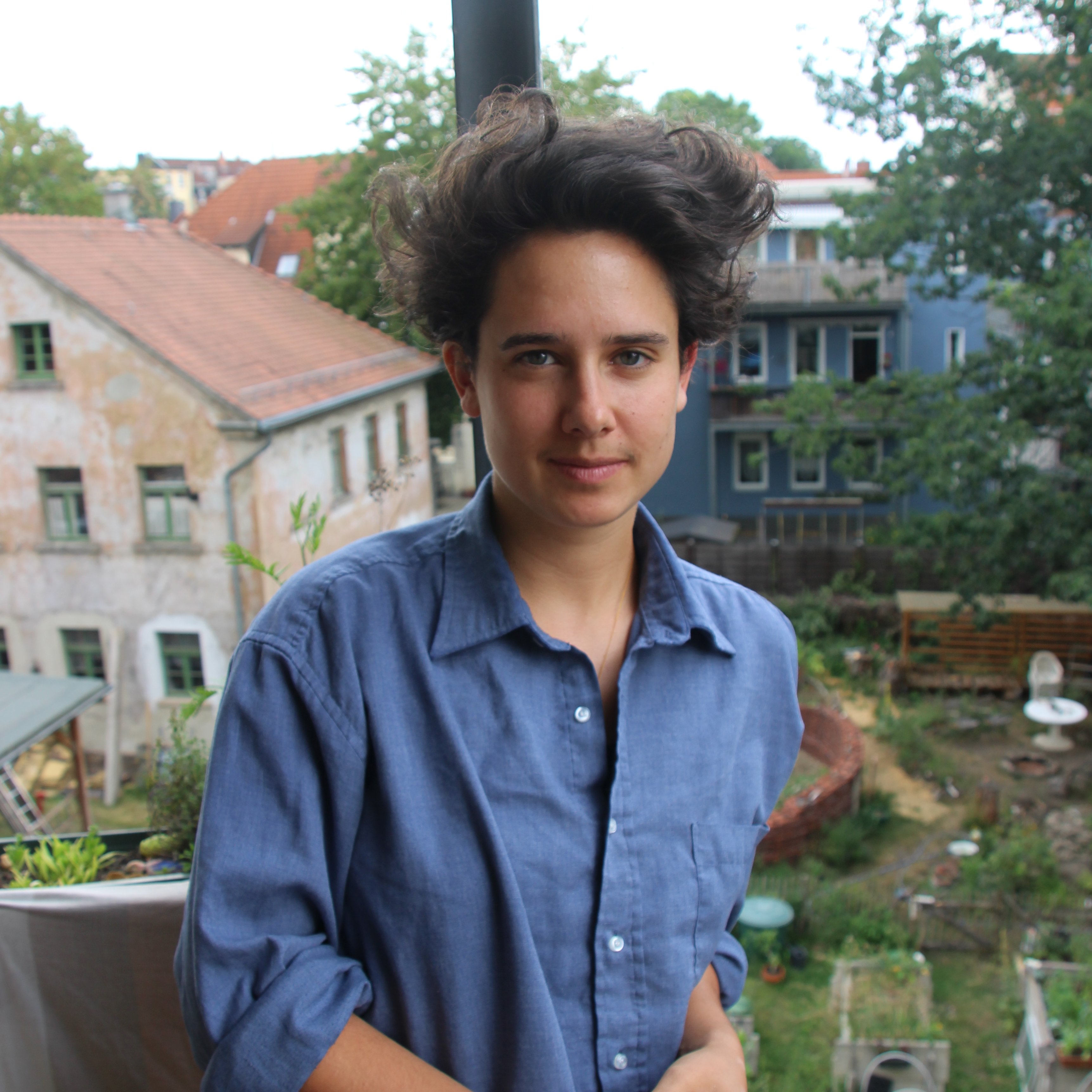 Olivia Golde lehnt sich an den Balkon und schaut frontal in die Kamera