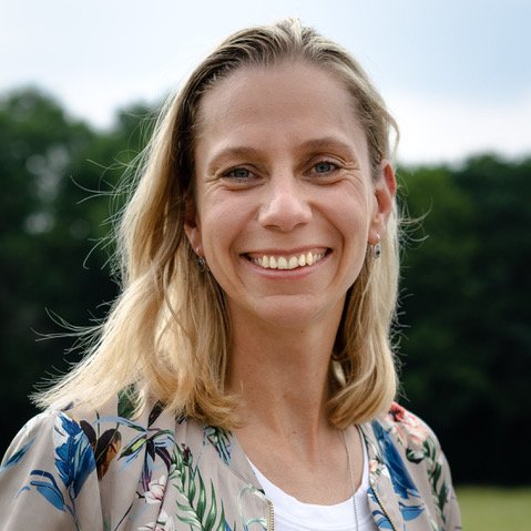 Katja Kramarczyk unter blauem Himmel mit einer grau-braunen Weste mit bunten Pflanzen aufdrucken