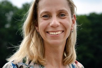Katja Kramarczyk unter blauem Himmel mit einer grau-braunen Weste mit bunten Pflanzen aufdrucken