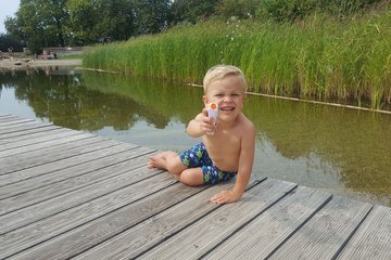Ein blondes Kind auf einem Steg mit Wasserpistole.