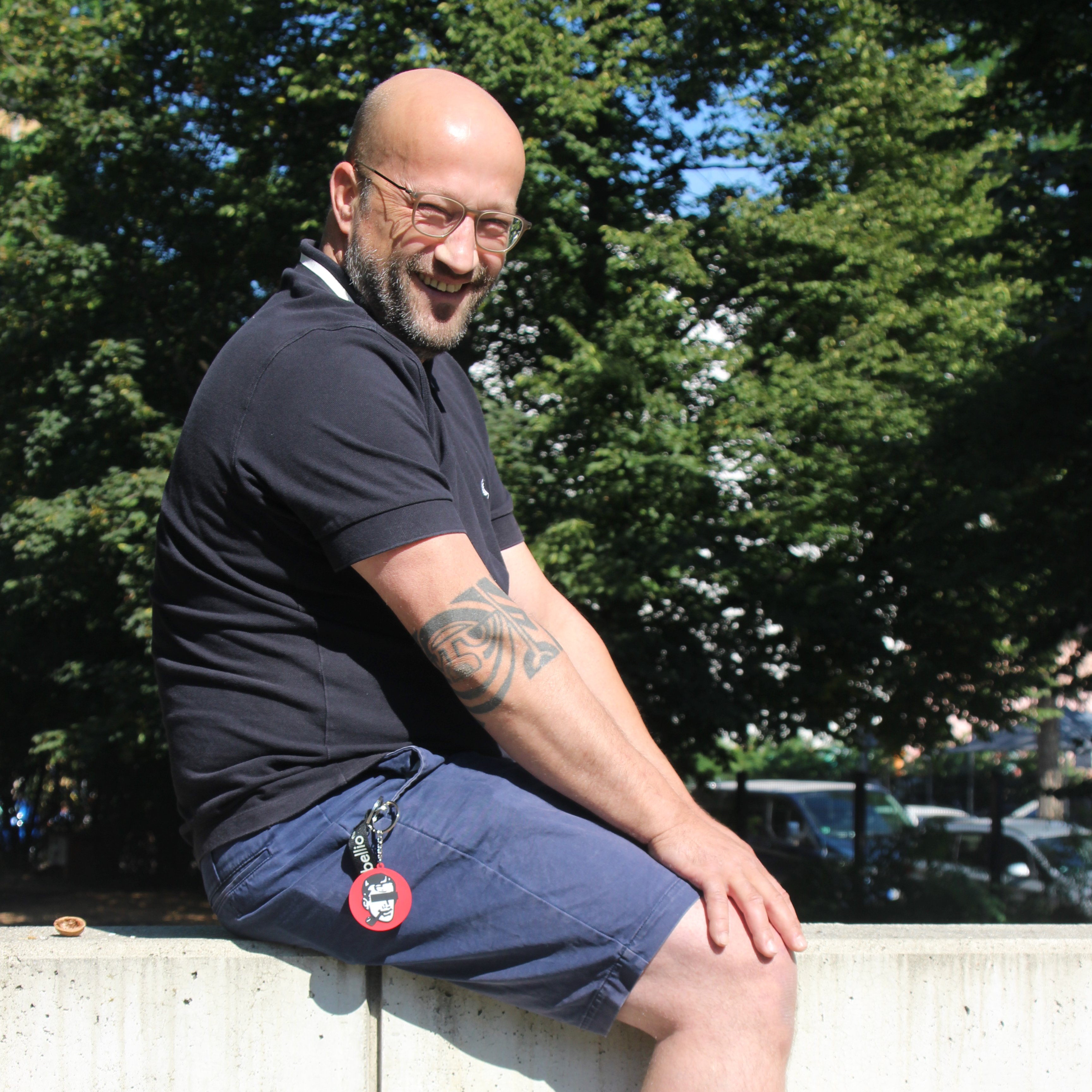 Jan Pallmer sitzt seitlich auf einer Mauer und grinst in die Kamera