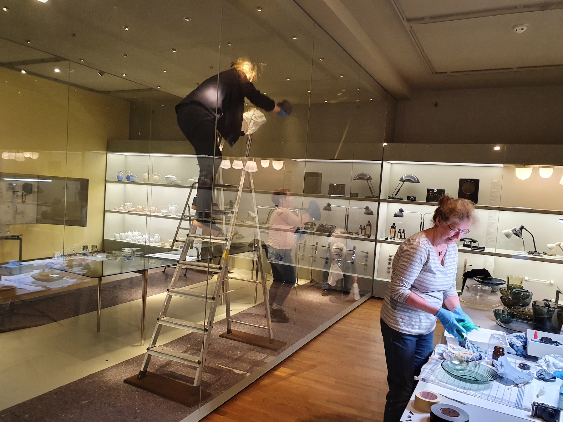 Moderne-Kuratorin Sabine Epple (auf der Leiter), Glas- und Keramikrestauratorin Ilona Faust (vorn) und Aufsichtspersonen bei der Reinigung der GRASSI-Sammlung
